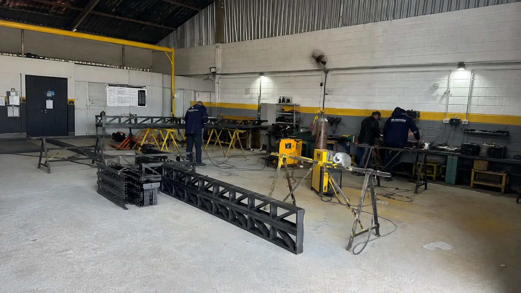 Oficina de fabricação com profissionais e estruturas metálicas em produção